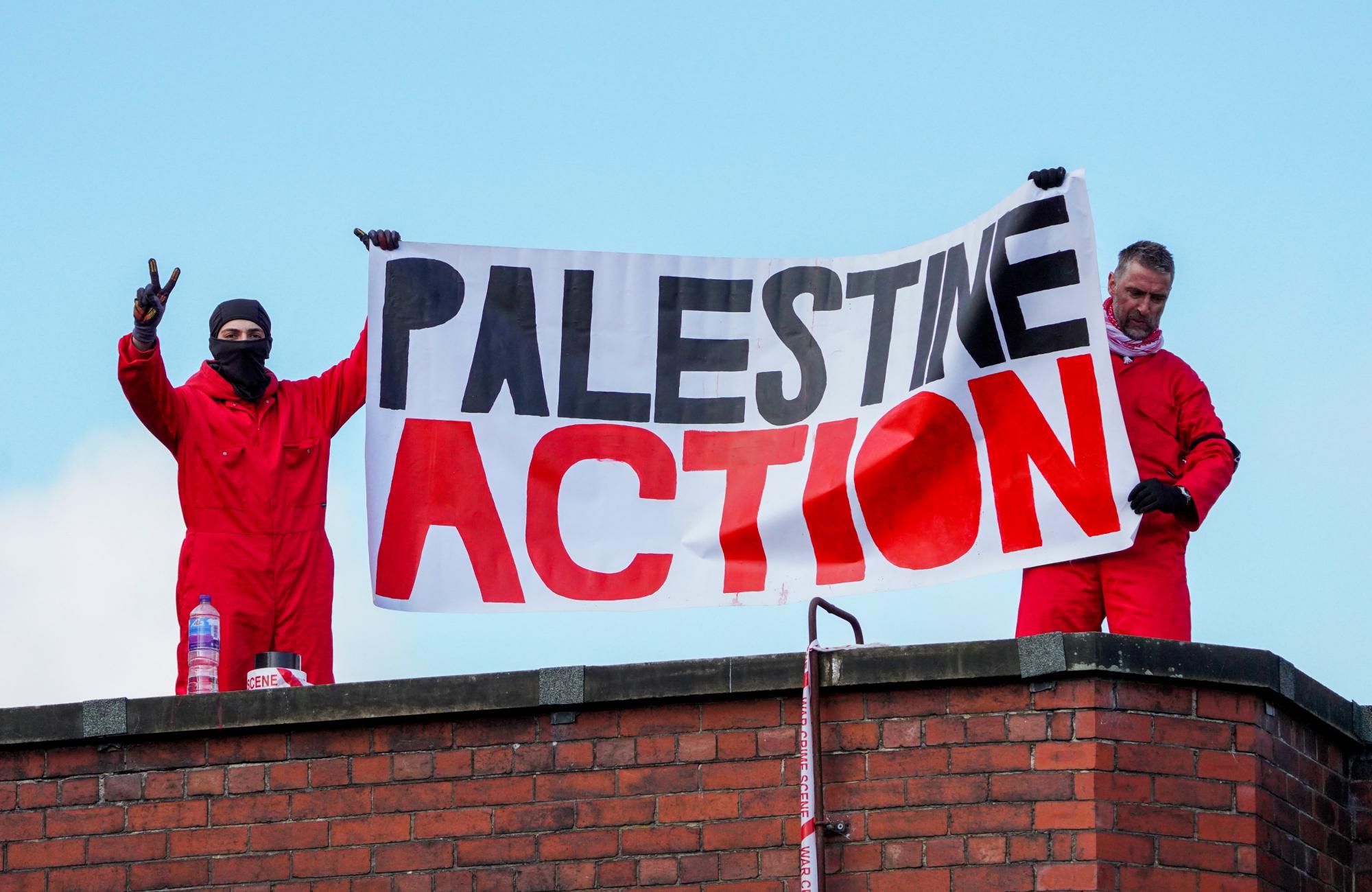 Twee mensen van Palestine Action dragen een banner bovenop het dak van een Elbit-fabriek.